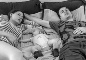 pareja en el sofá o en la cocina con gesto de agotamiento, bebé cerca